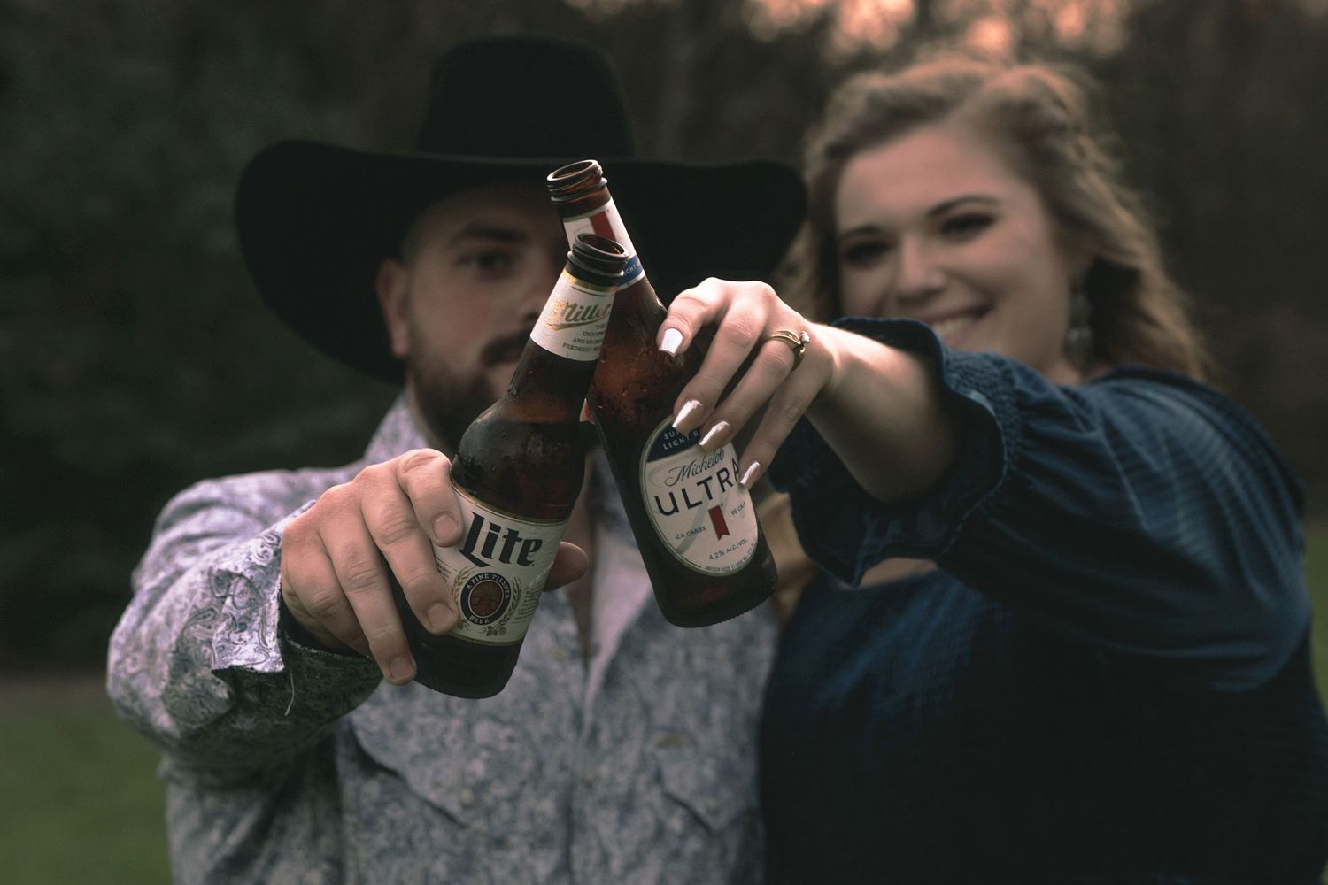 A celebratory toast with beer bottles in a country setting at sunset.