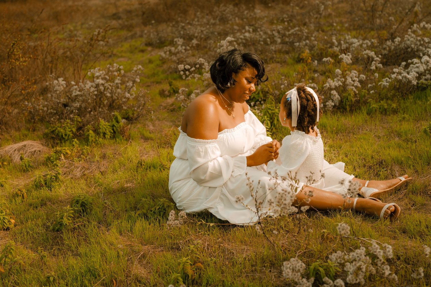 A heartwarming outdoor portrait of two people in white dresses sitting together in a meadow.