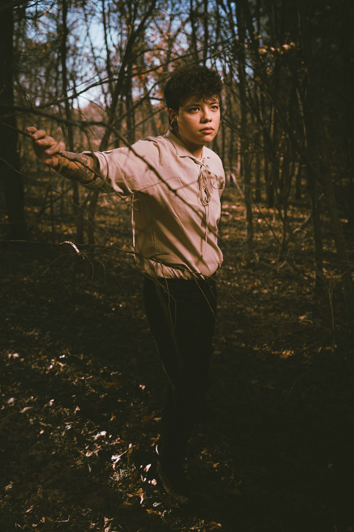 Vintage-styled portrait of person in tan shirt posing in autumn forest.