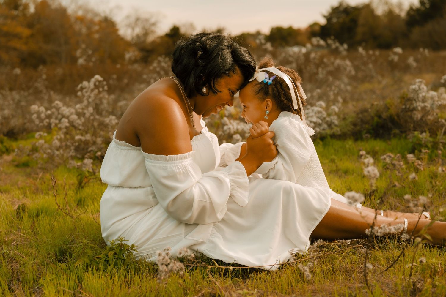 Intimate portrait of two people in white dresses sitting in a sunlit meadow.