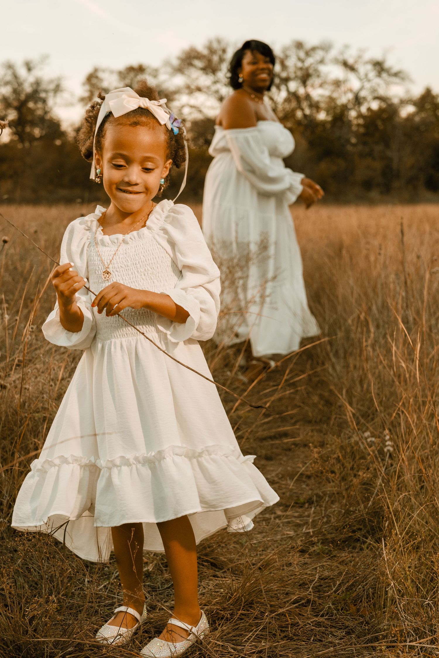 A joyful outdoor portrait featuring two people in white dresses against a warm autumn backdrop.