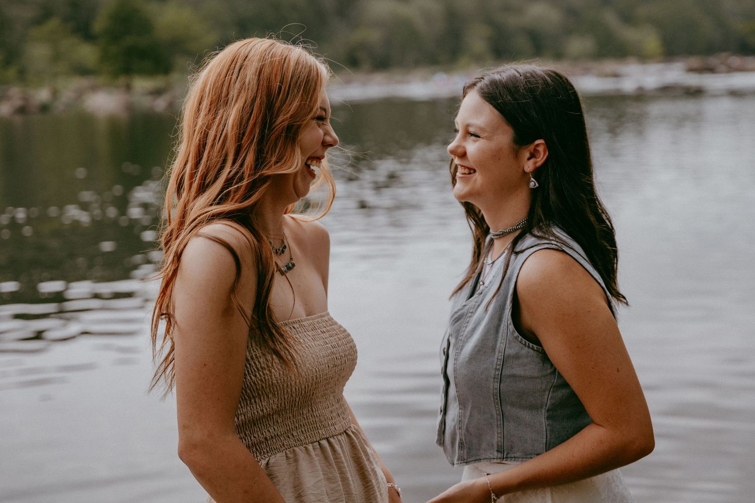 Two people laugh together while sitting by a serene lake on a sunny afternoon.