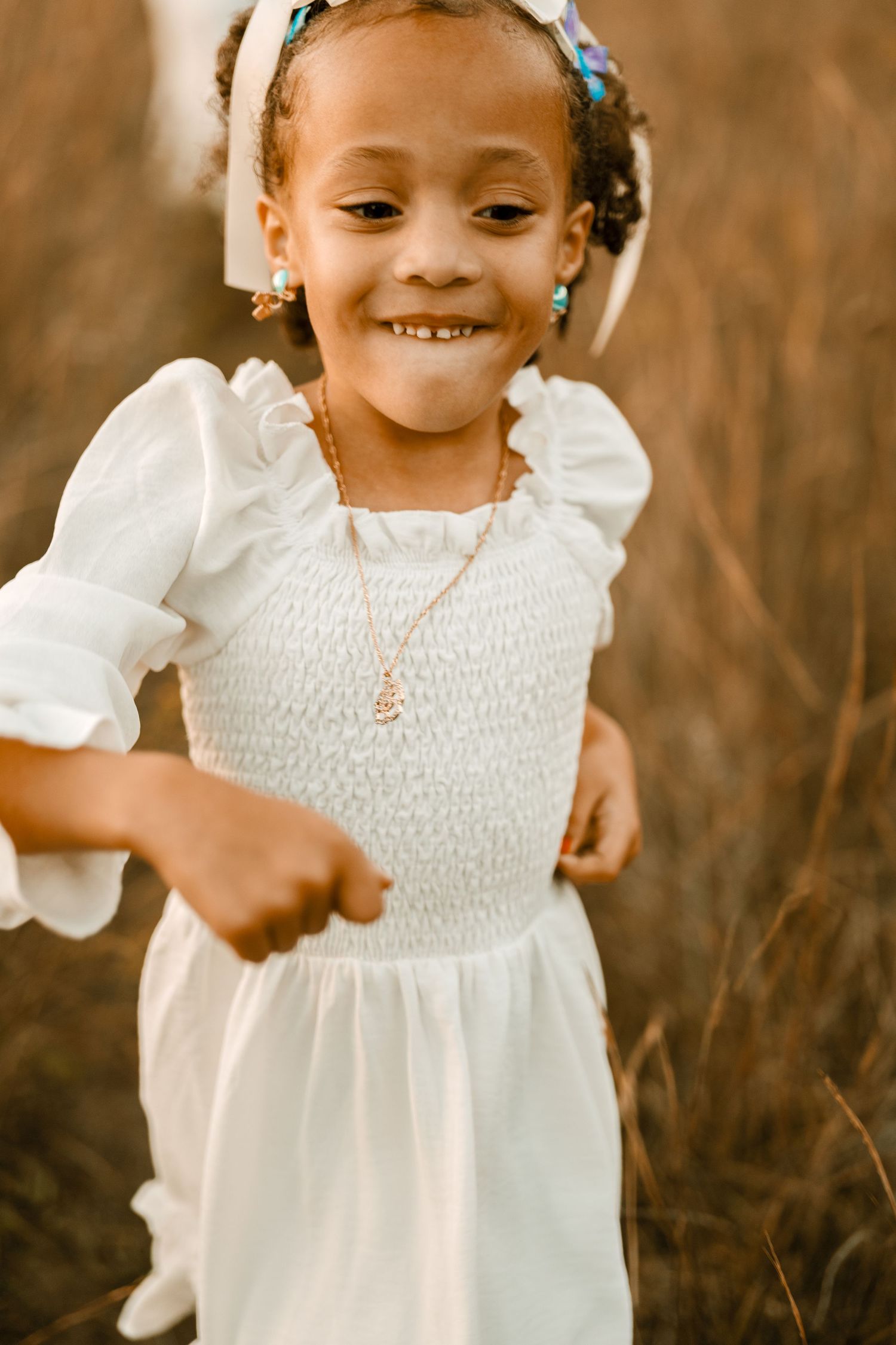 A cheerful child wearing a white smocked dress poses during a golden hour portrait session.