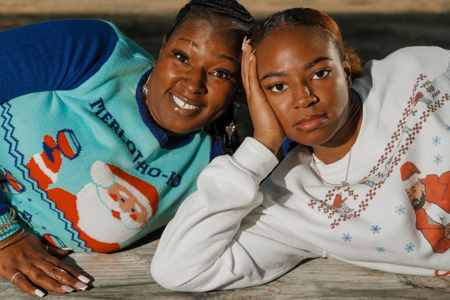Two people wearing Christmas sweaters with Santa designs pose together outdoors.