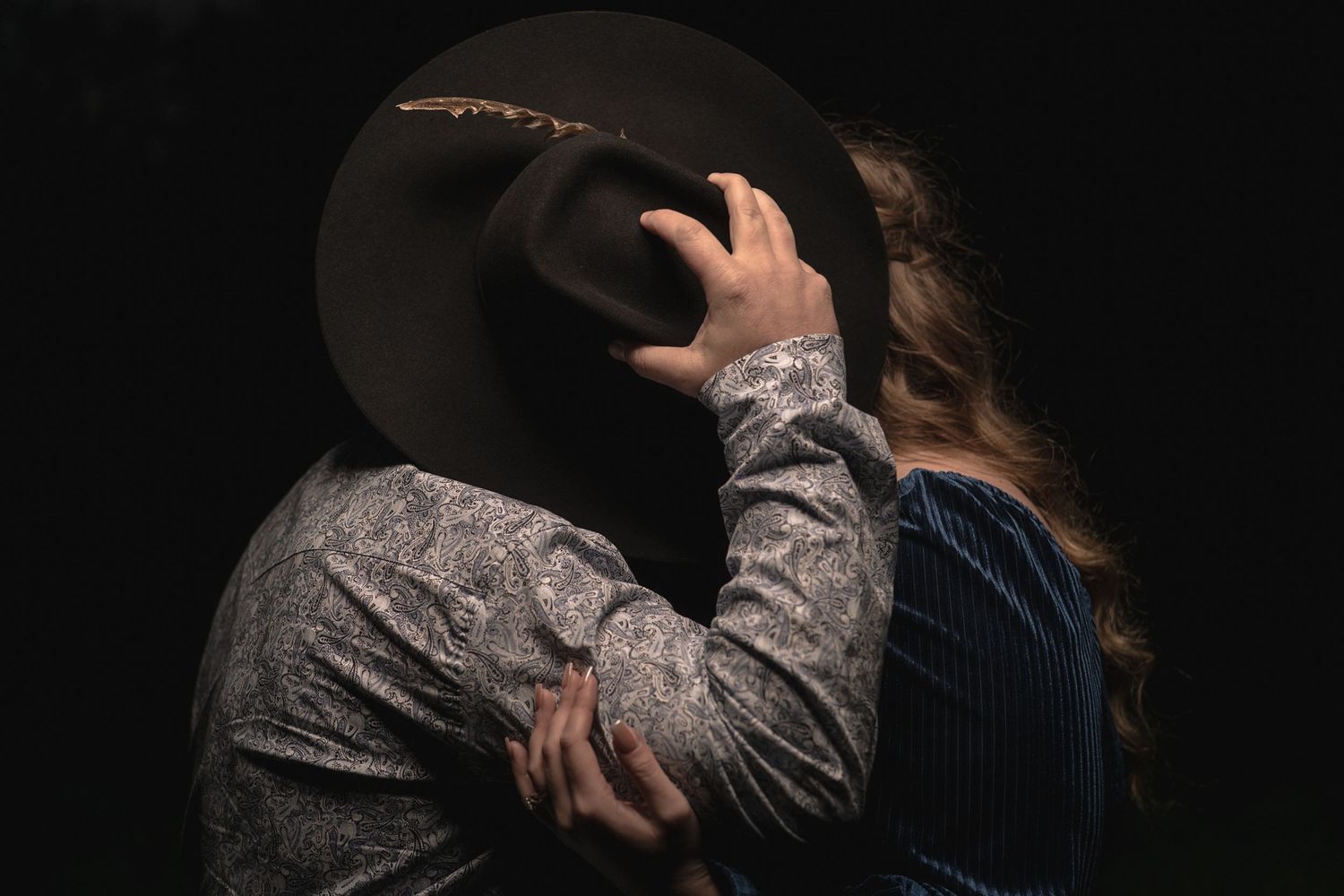 Person in western attire adjusts their hat against a dark background.