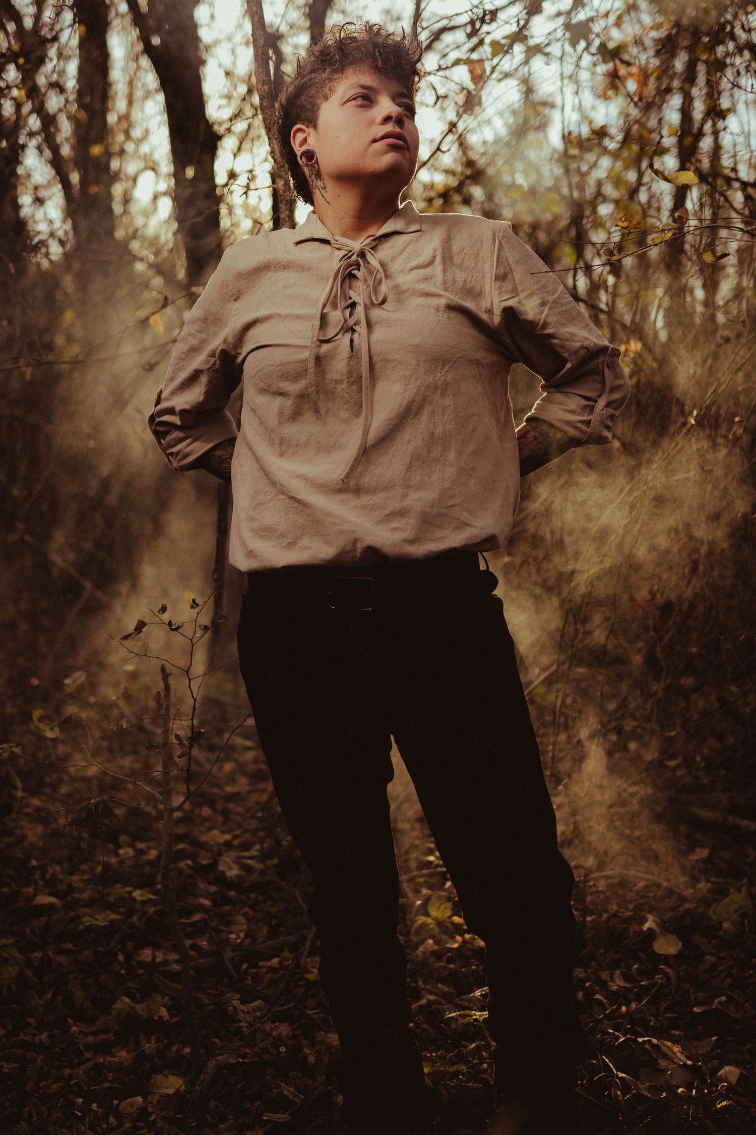 A figure in vintage-style clothing poses dramatically against an autumn woodland backdrop.
