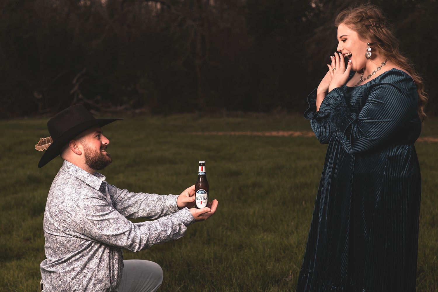 A rustic outdoor proposal scene with a cowboy kneeling and holding out a ring.