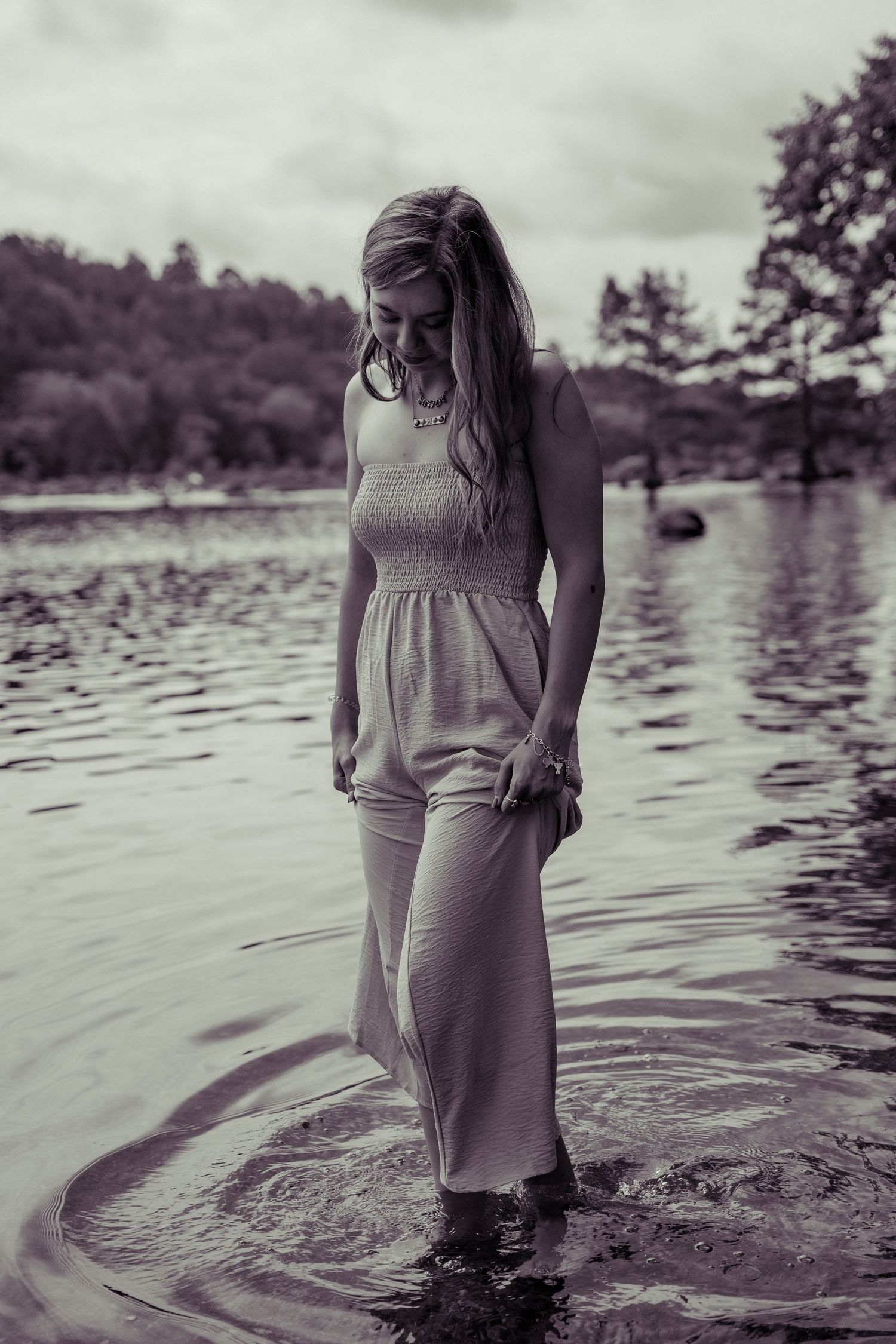 Black and white photographs capture an ethereal moment as a figure in a dress wades through rippling lake water.