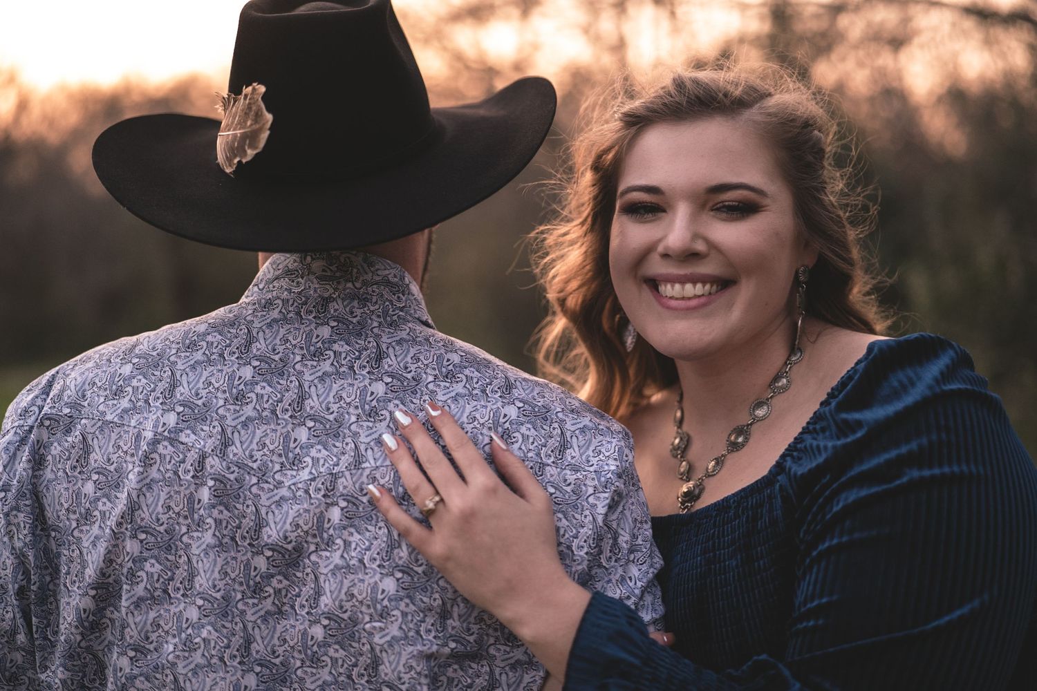 Couple in western attire sharing joyful moment during sunset engagement shoot.