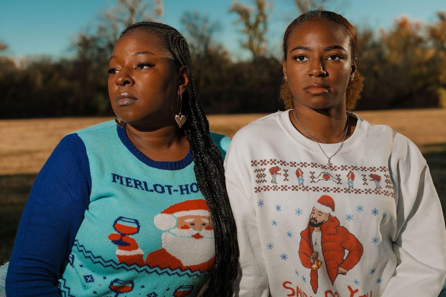 Two people in coordinating holiday sweaters pose against autumn field backdrop.