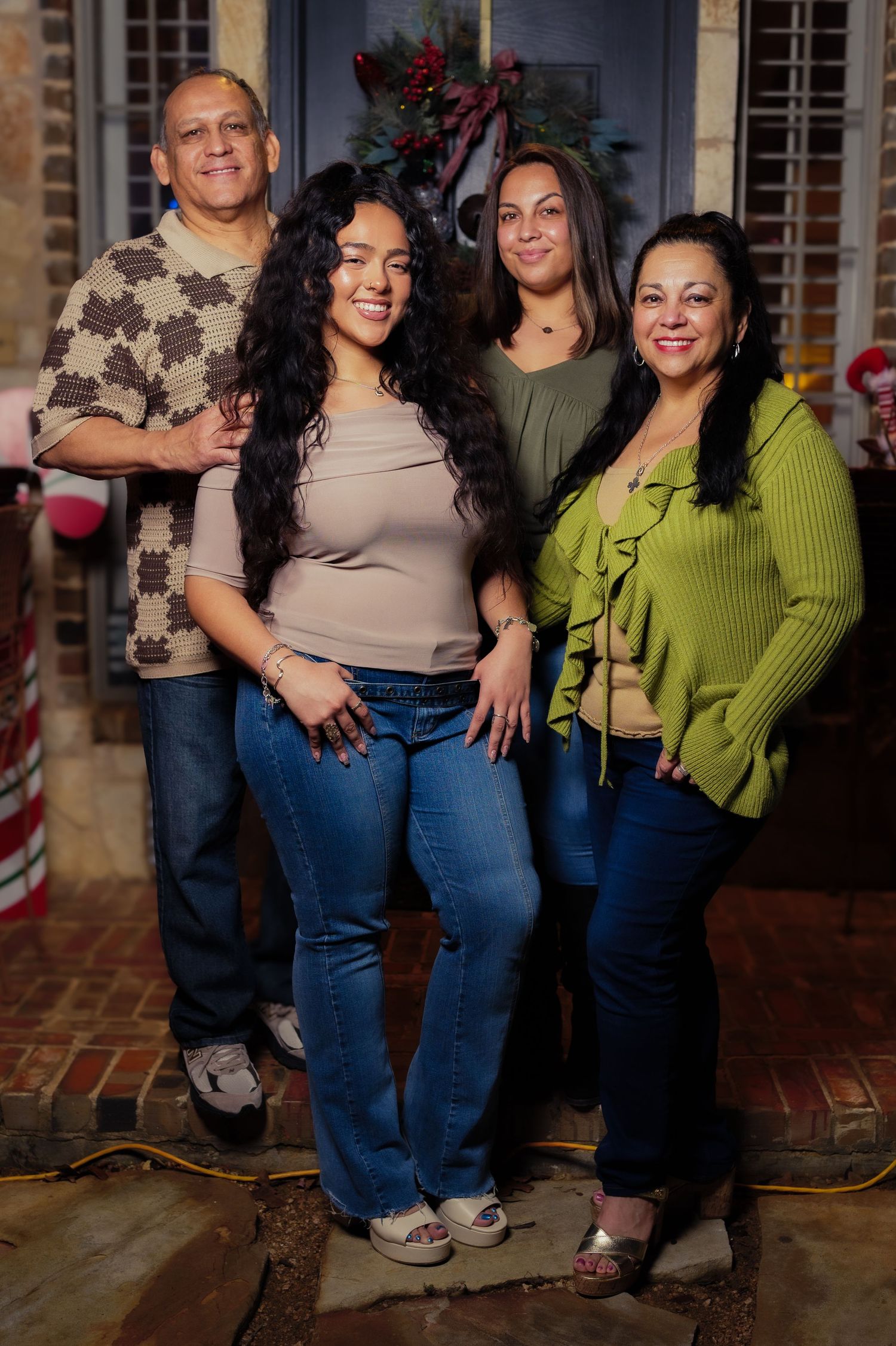 Family portrait of four people standing on brick porch with festive front door.