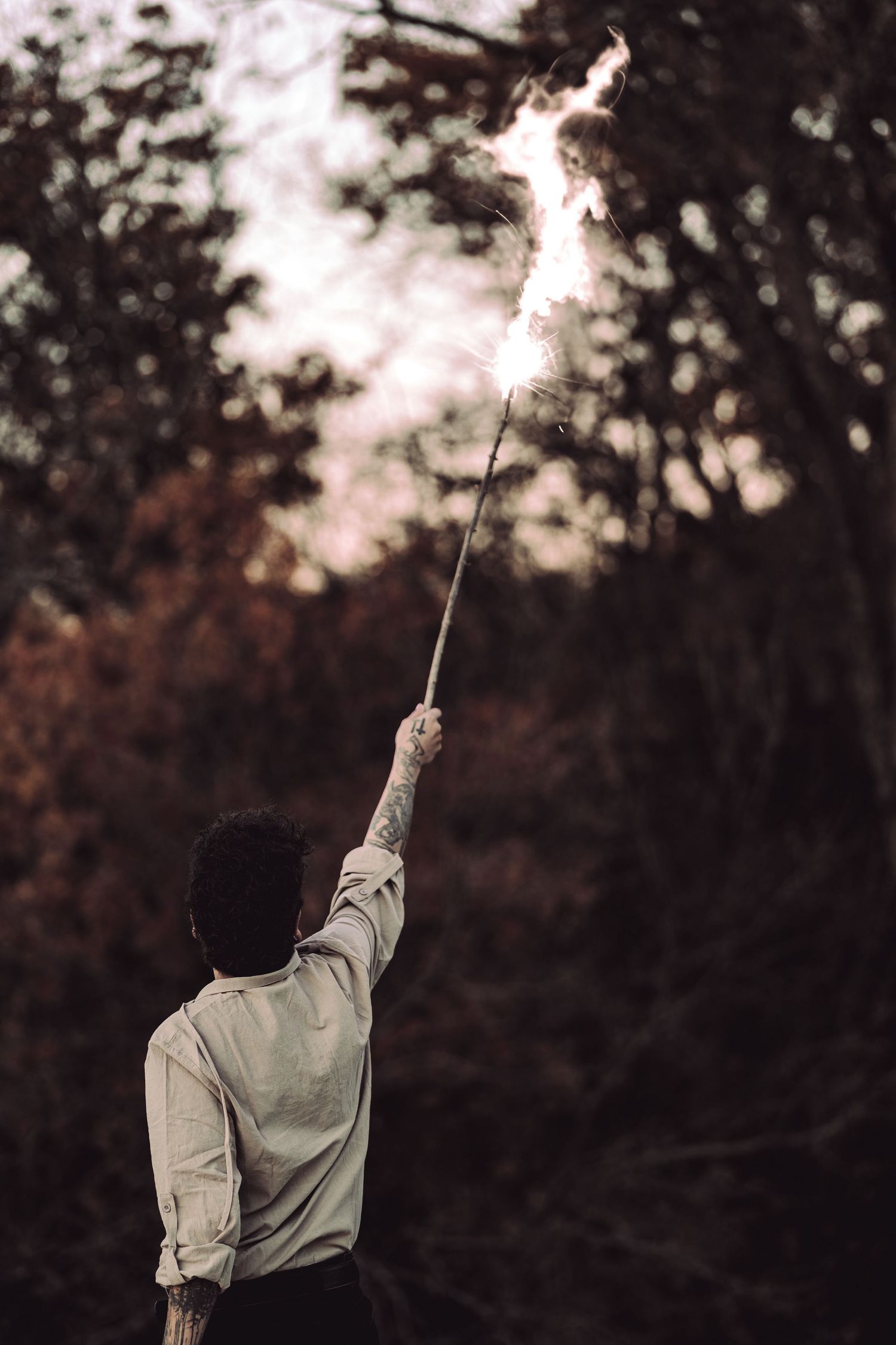 Silhouette holding a sparkler against twilight sky in woods.