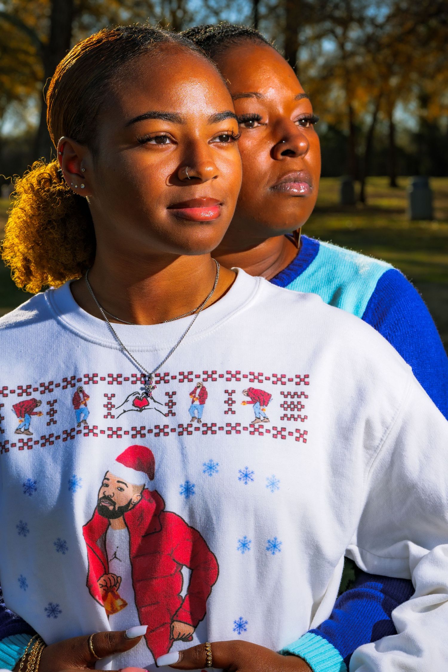 Two people wearing winter sweaters pose together in warm sunlight outdoors.
