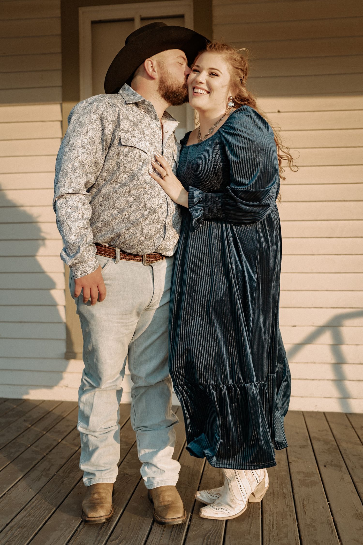 A sweet moment captured on a wooden porch with western-styled clothing and cowboy attire.
