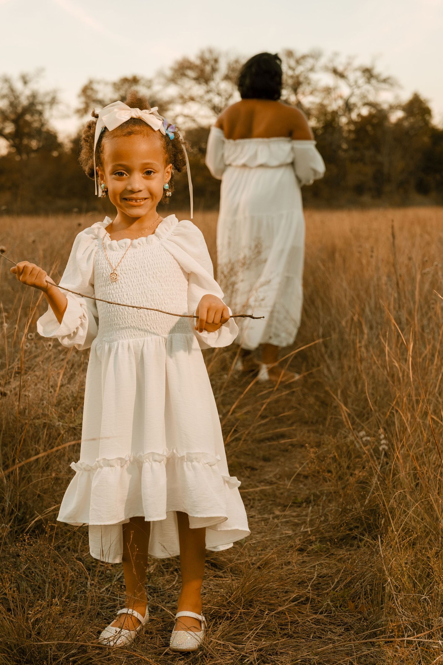 A sweet outdoor portrait in a golden field with two people wearing matching white dresses.
