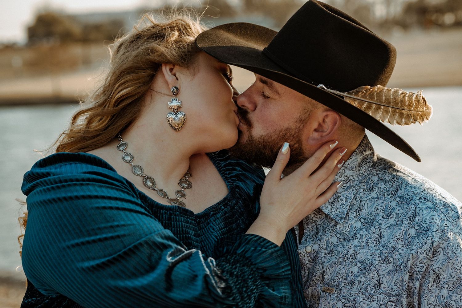 A romantic western-styled couple sharing an intimate kiss outdoors.