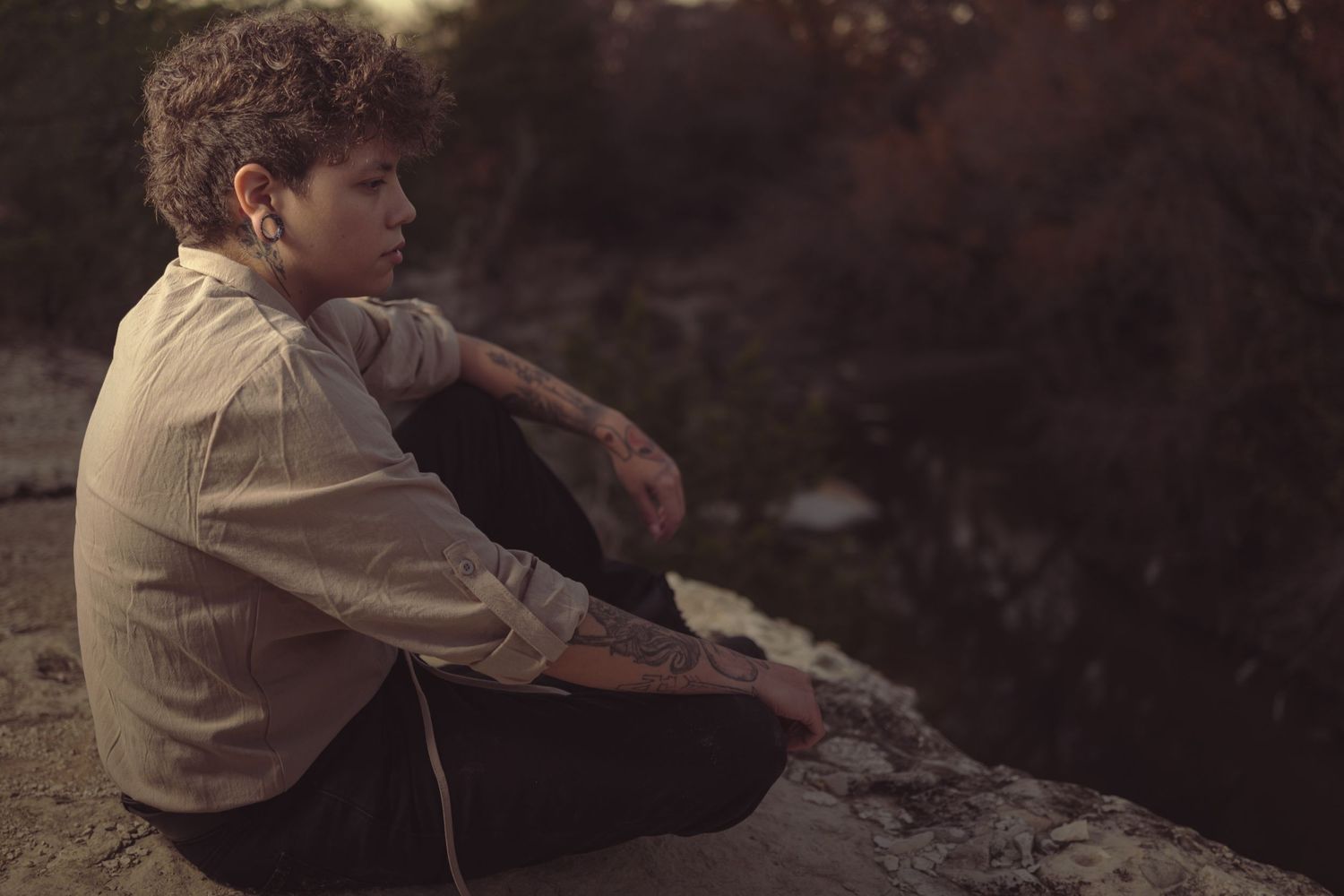 A contemplative figure in vintage clothing sitting on rocks at dusk.