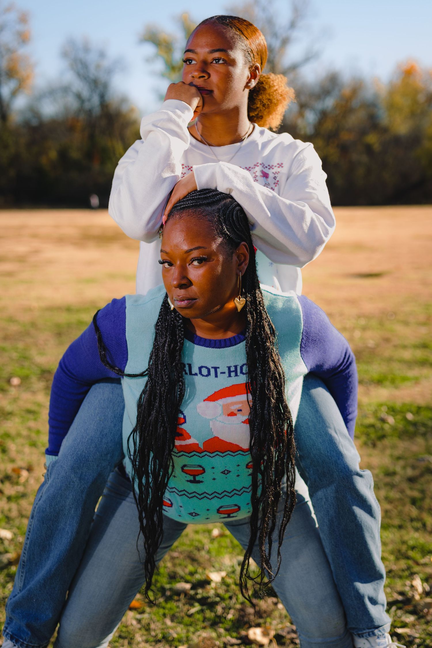 Two people wearing holiday sweaters pose together in a field during golden hour.