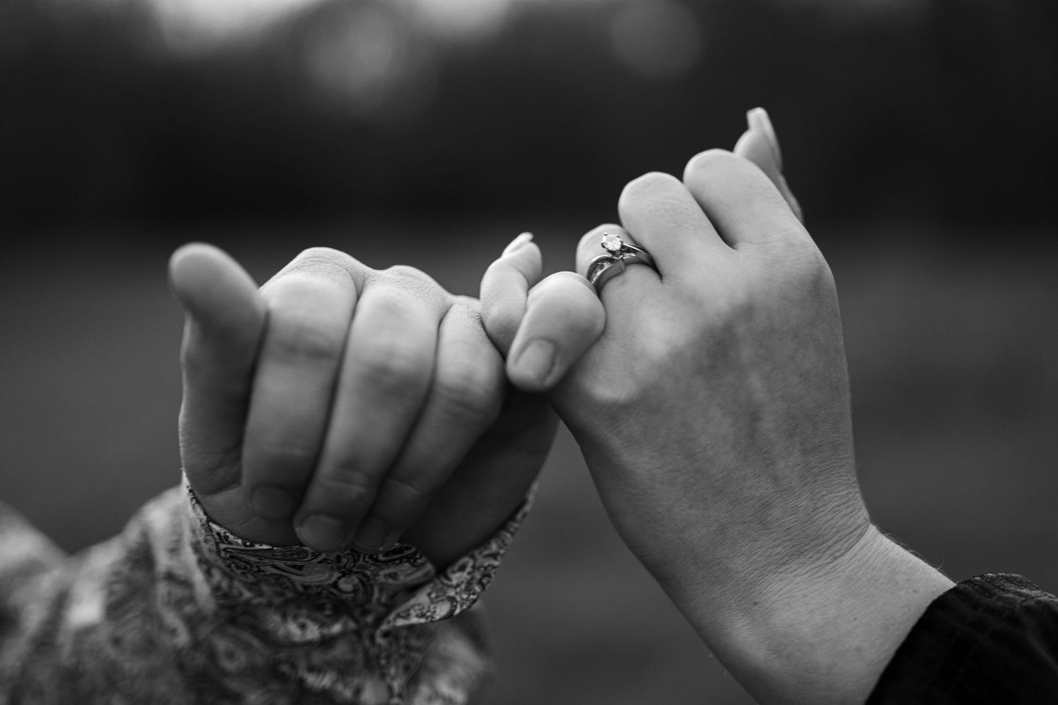 Two hands making a pinky promise against a blurred background in black and white.