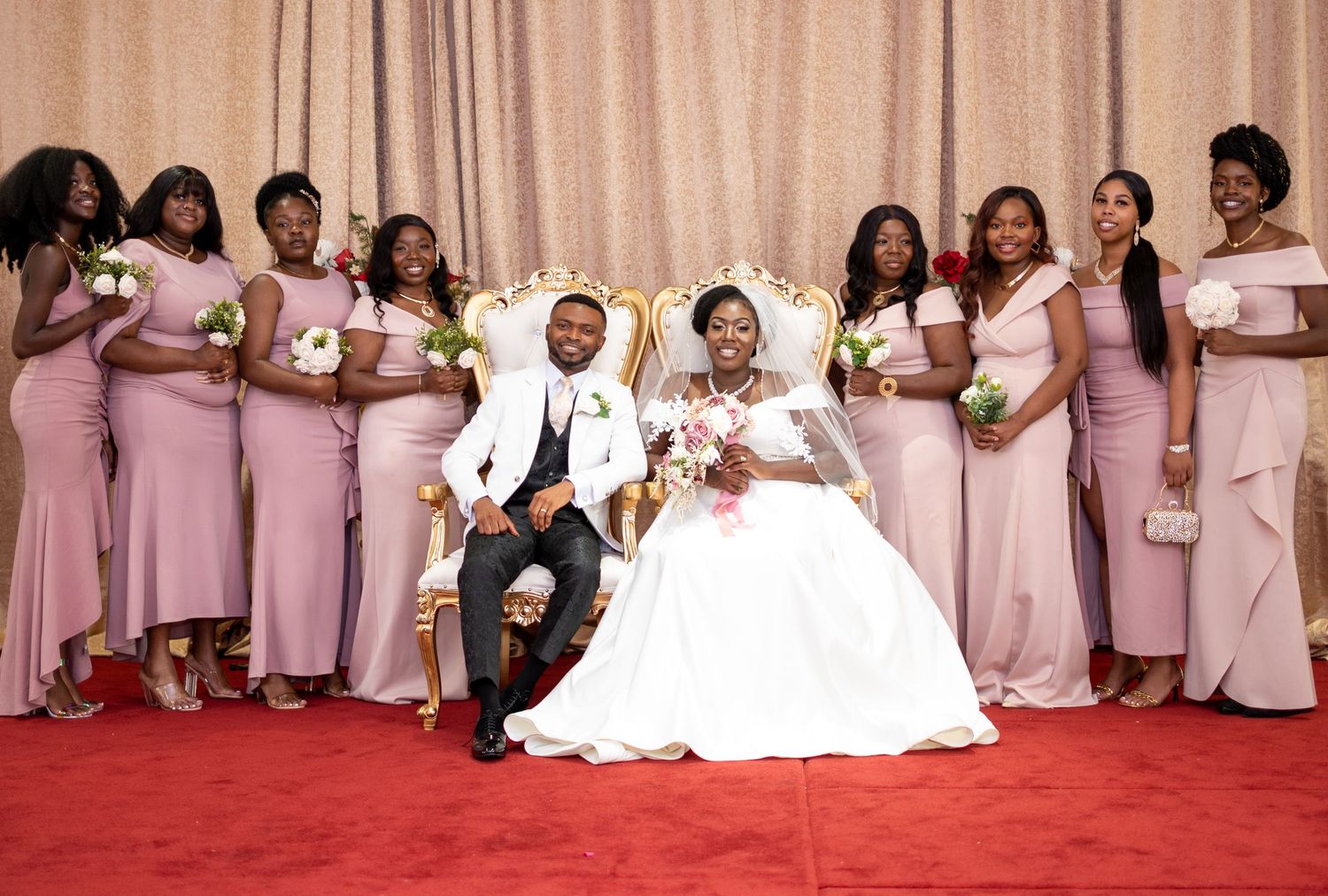 Wedding party poses together on red carpet with couple in center wearing white dress and black suit with pink bridesmaids.