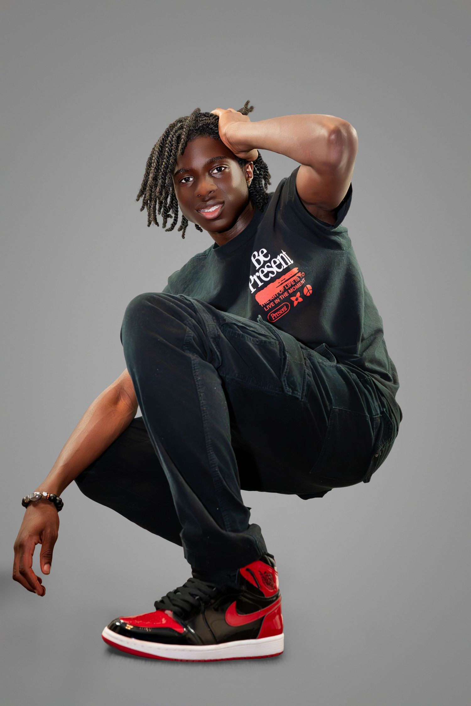 Dynamic portrait of dancer in black streetwear and red Air Jordan sneakers posing against grey background.