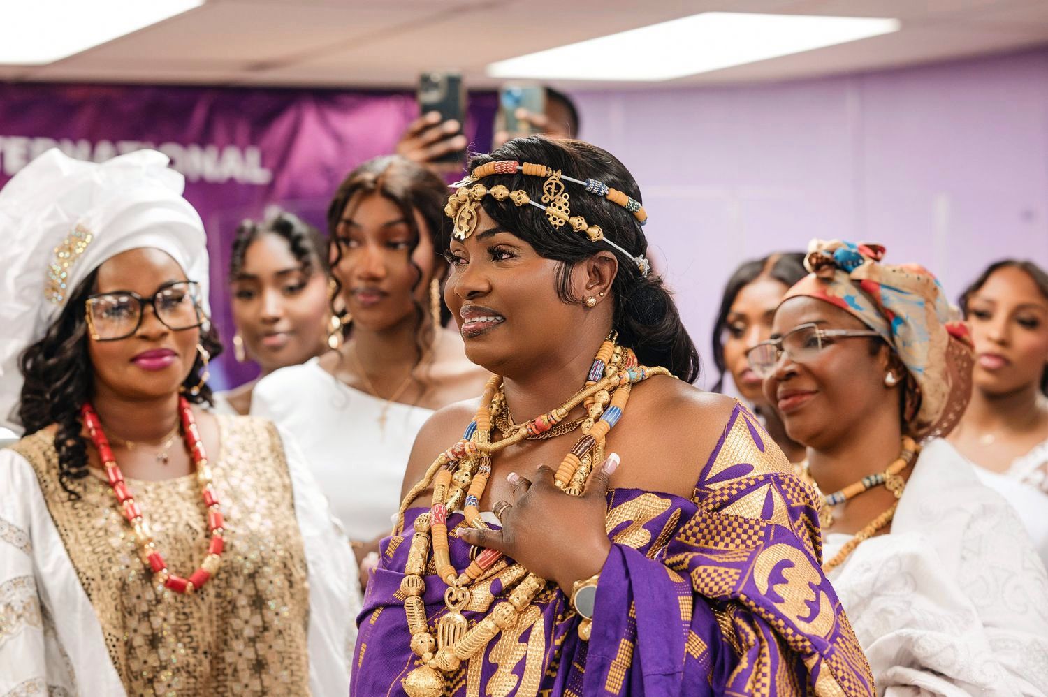 Celebrants wearing vibrant traditional African attire and colorful head wraps gather together at an indoor celebration.