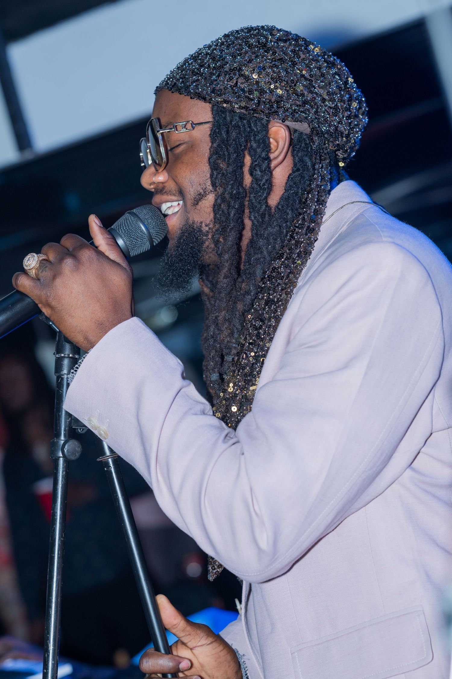 Performer with braided hair and glasses sings emotively while holding microphone on stage.