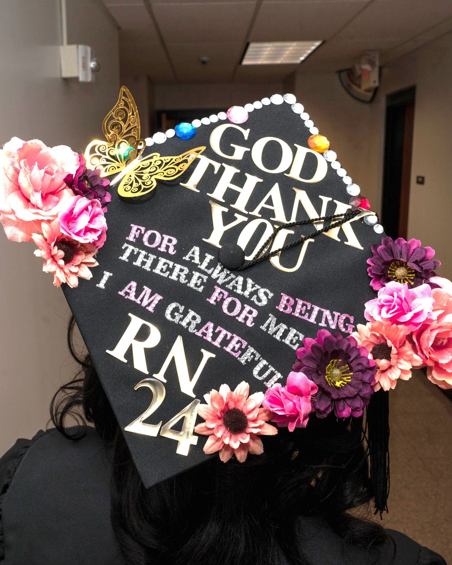 A decorated graduation cap with floral designs reads 'God Thank You' and 'RN 24'.