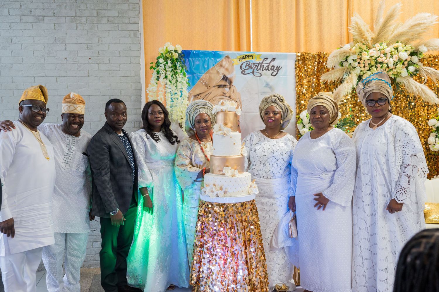 Wedding celebration with guests in traditional white Nigerian attire posing with a decorated cake.