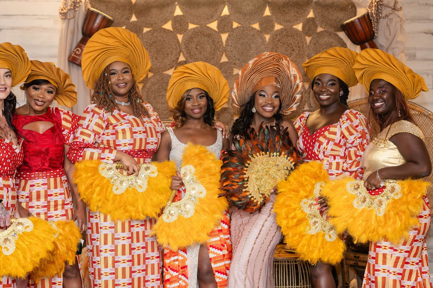 A group in coordinated yellow and white outfits with matching yellow feather fans pose together at a celebration.