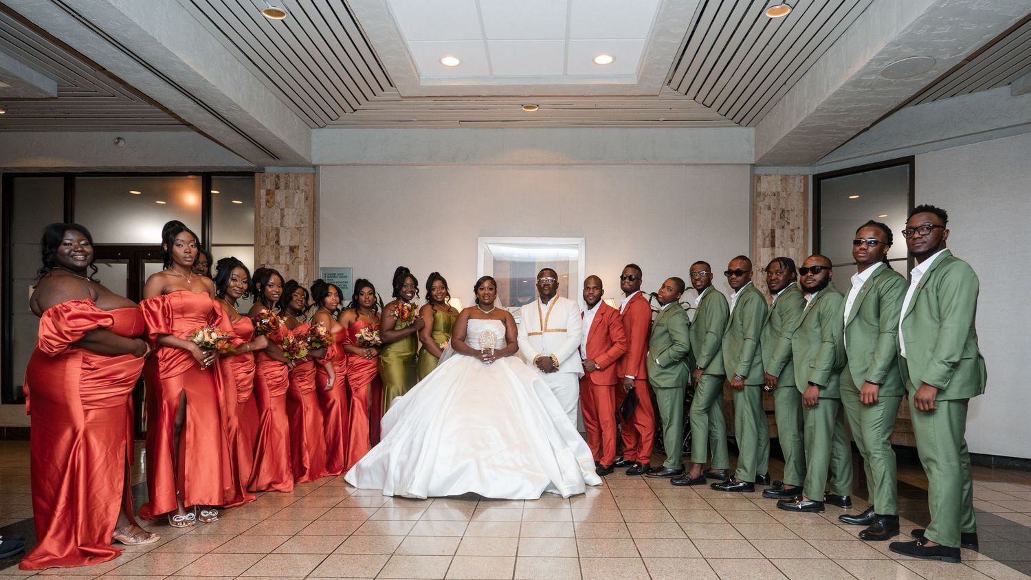 Wedding party poses in vibrant red and green attire with the newlyweds in the center.