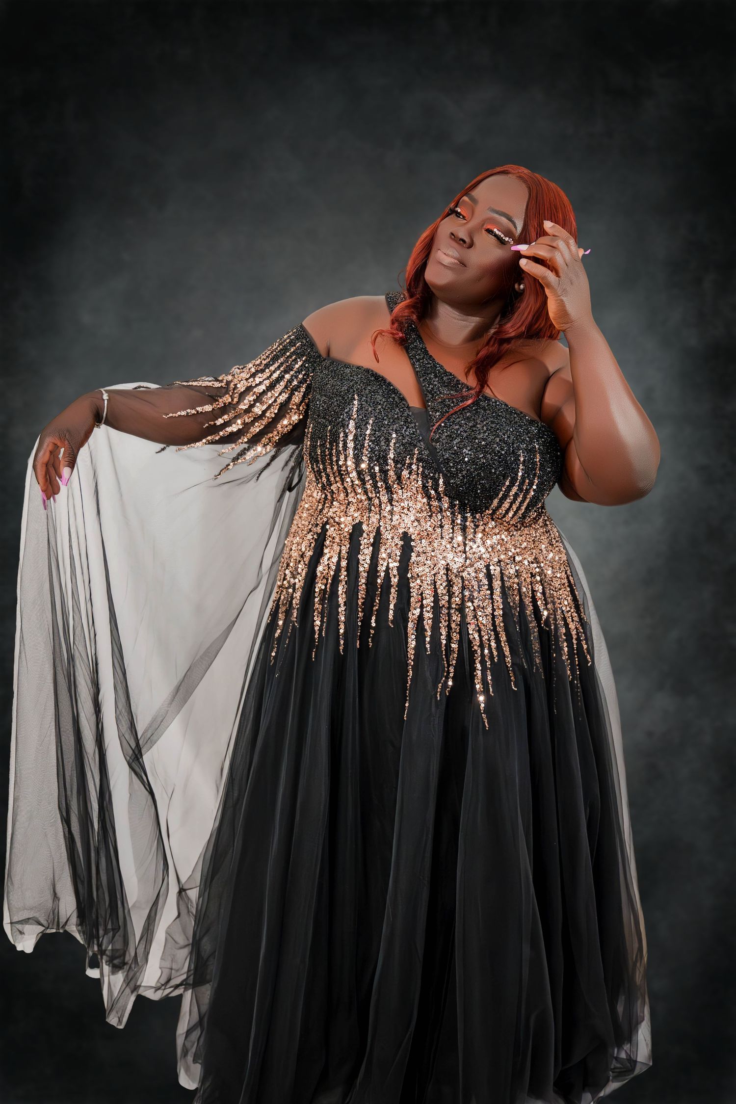 A woman in a flowing black evening gown with gold sequin details poses elegantly against a dark backdrop.