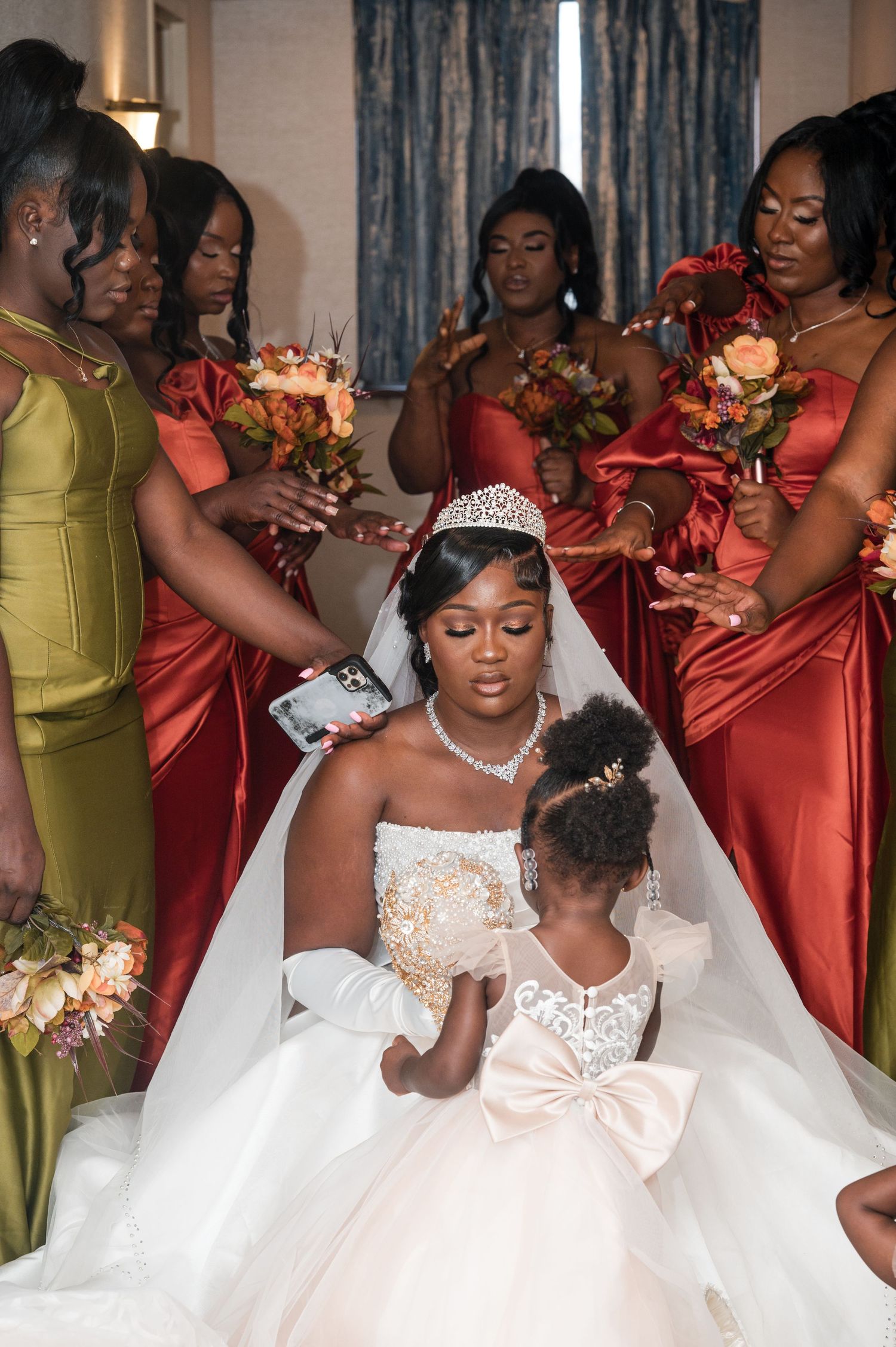 A wedding party surrounds the bride and flower girl, wearing coral dresses and holding bouquets.
