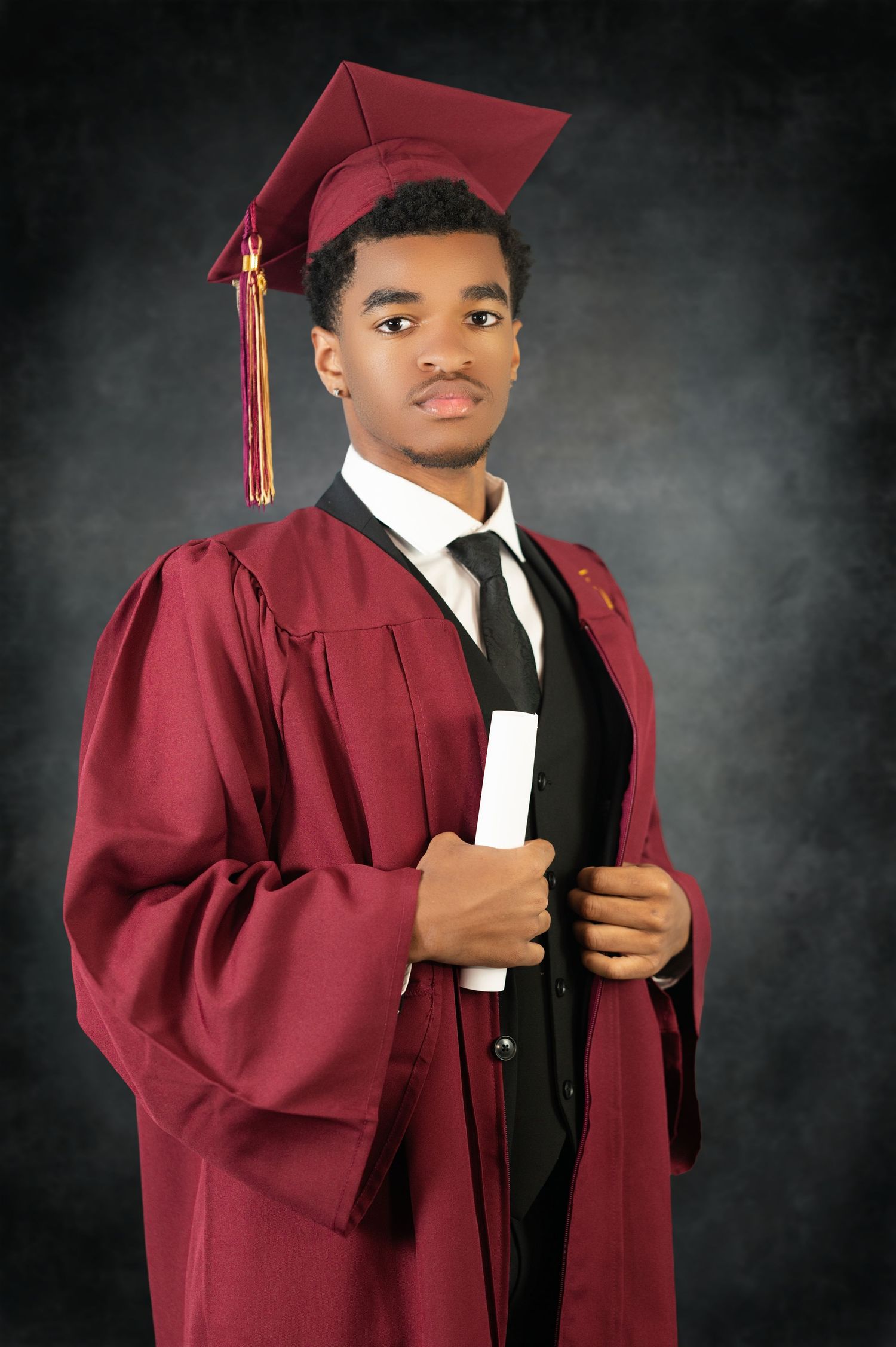 A graduate in a maroon cap and gown with black tie poses for a formal portrait against a dark background.