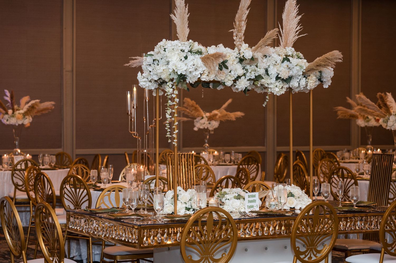 Elegant wedding reception table with gold chairs and tall white floral centerpiece arrangements in luxury venue.