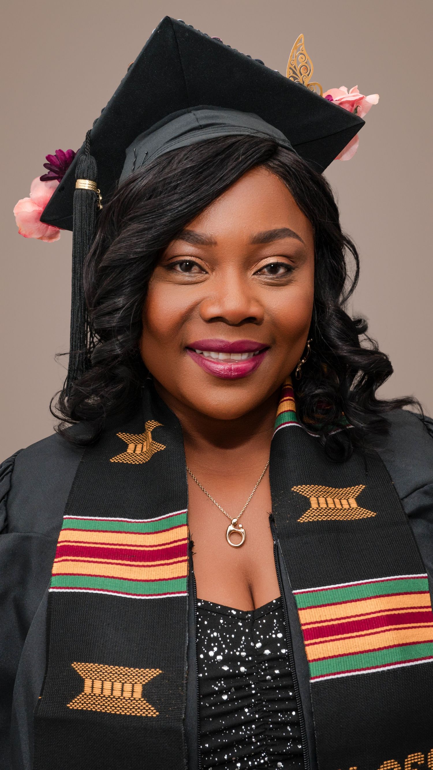 Graduate wearing a black cap and gown with colorful kente stole smiles during commencement ceremony portrait.