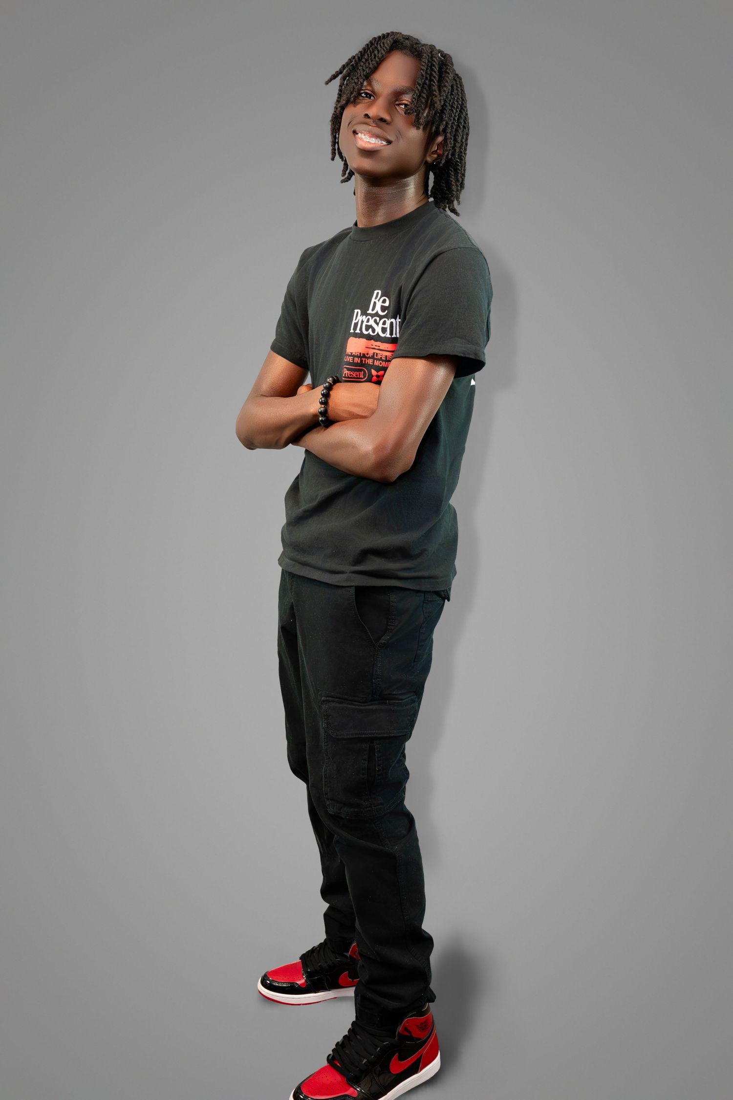 A person wearing a dark t-shirt and cargo pants poses confidently against a grey background while wearing red and black sneakers.