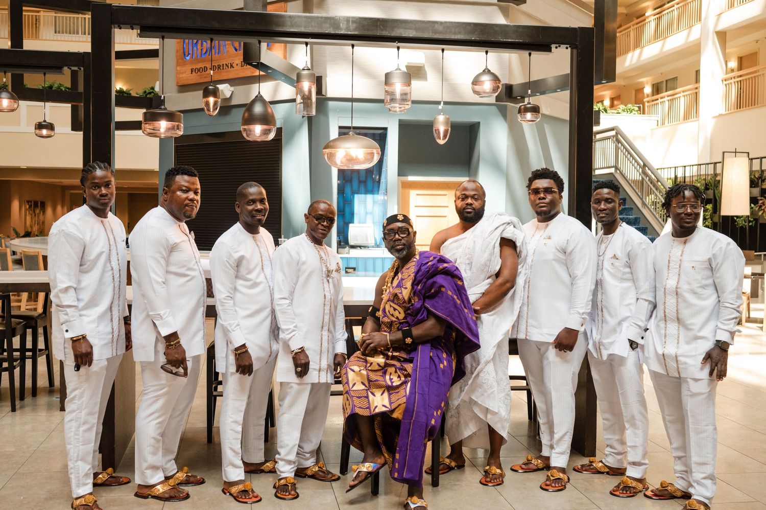 Wedding party in all white suits poses indoors with purple accent attire.