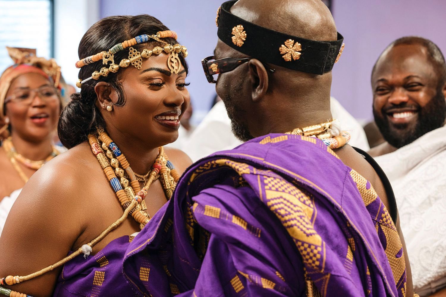 Traditional African wedding celebration with couple in ornate gold and purple attire sharing a joyful moment.