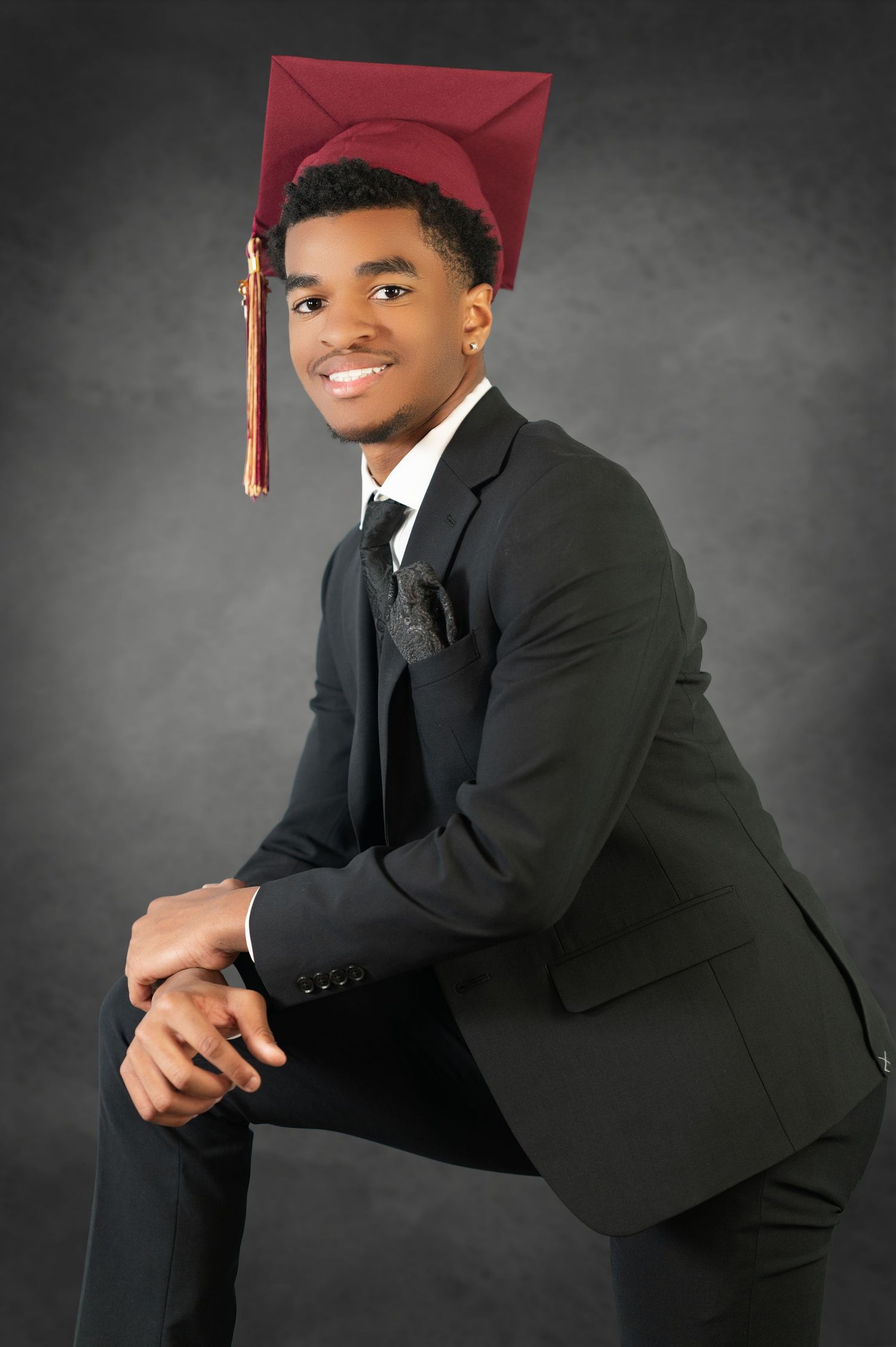 Graduation portrait of a graduate in a black suit and red cap posing against a grey backdrop.