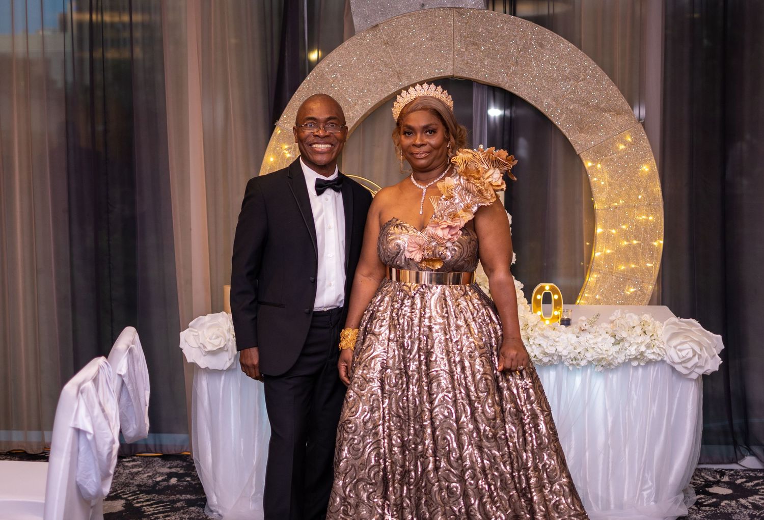 A couple poses under a sparkly archway at a formal celebration.