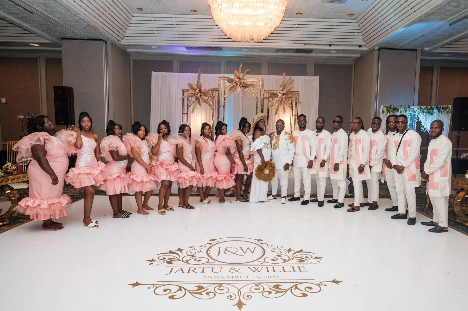 Wedding party members wearing blush pink and white outfits pose with a decorative floor design.