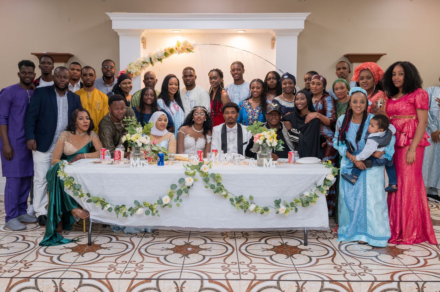 Group photo at an elegant formal event with decorated head table featuring white floral garlands and candles.