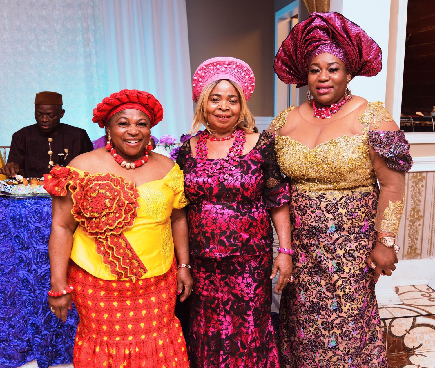 Women in colorful traditional African dresses and headwraps pose at formal celebration.