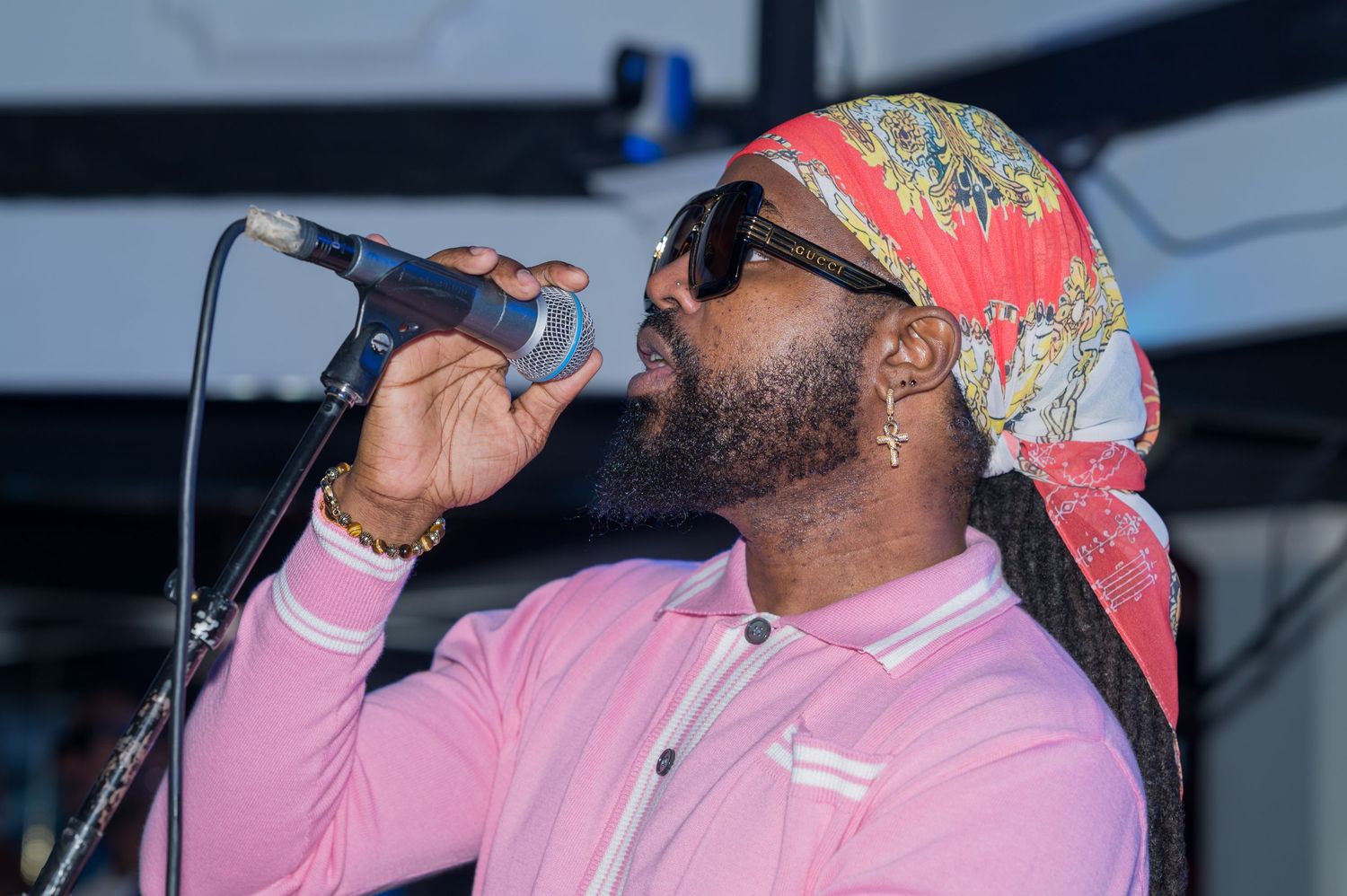 Singer in pink attire and colorful headwrap performs with emotion on stage.