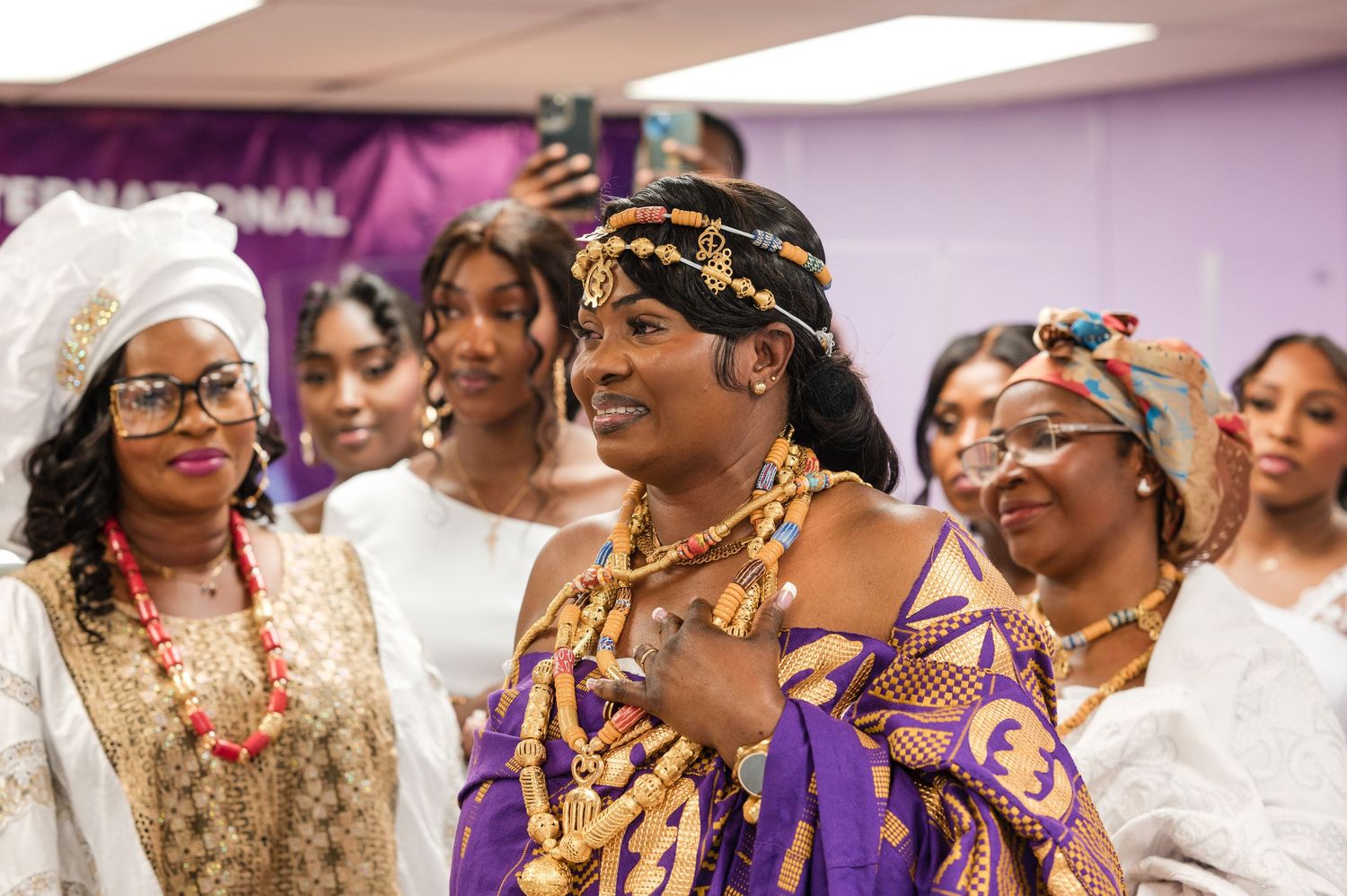 A group of people wearing traditional African and formal attire gather together at an indoor celebration event.