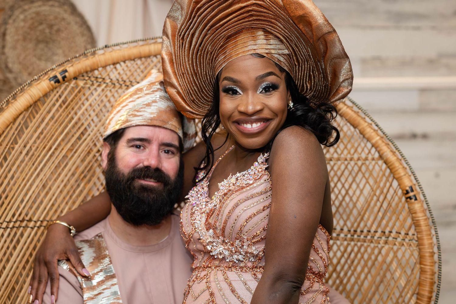 Couple poses in wedding attire featuring traditional gele and peacock chair.