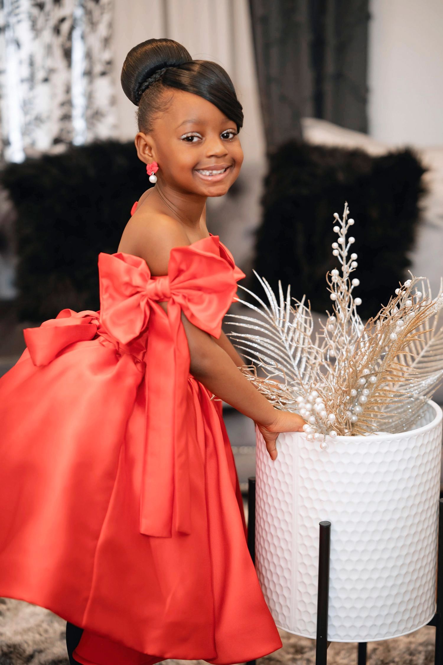 Fancy coral-colored party dress with large bow detail styled with silver holiday decor against dark background.