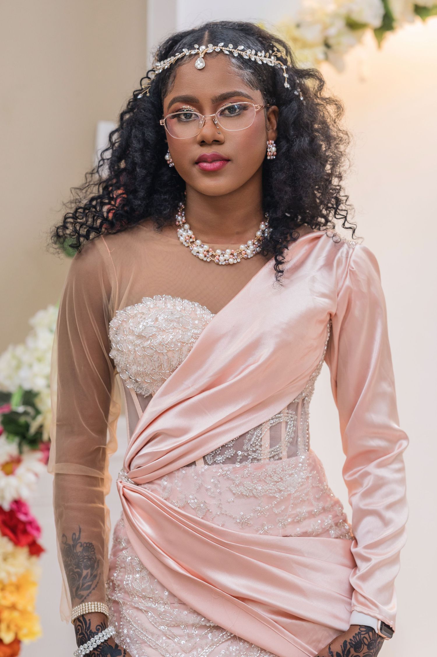 Beautiful bride wearing round glasses, curly hair, crystal headpiece and blush pink draped wedding gown with lace details.