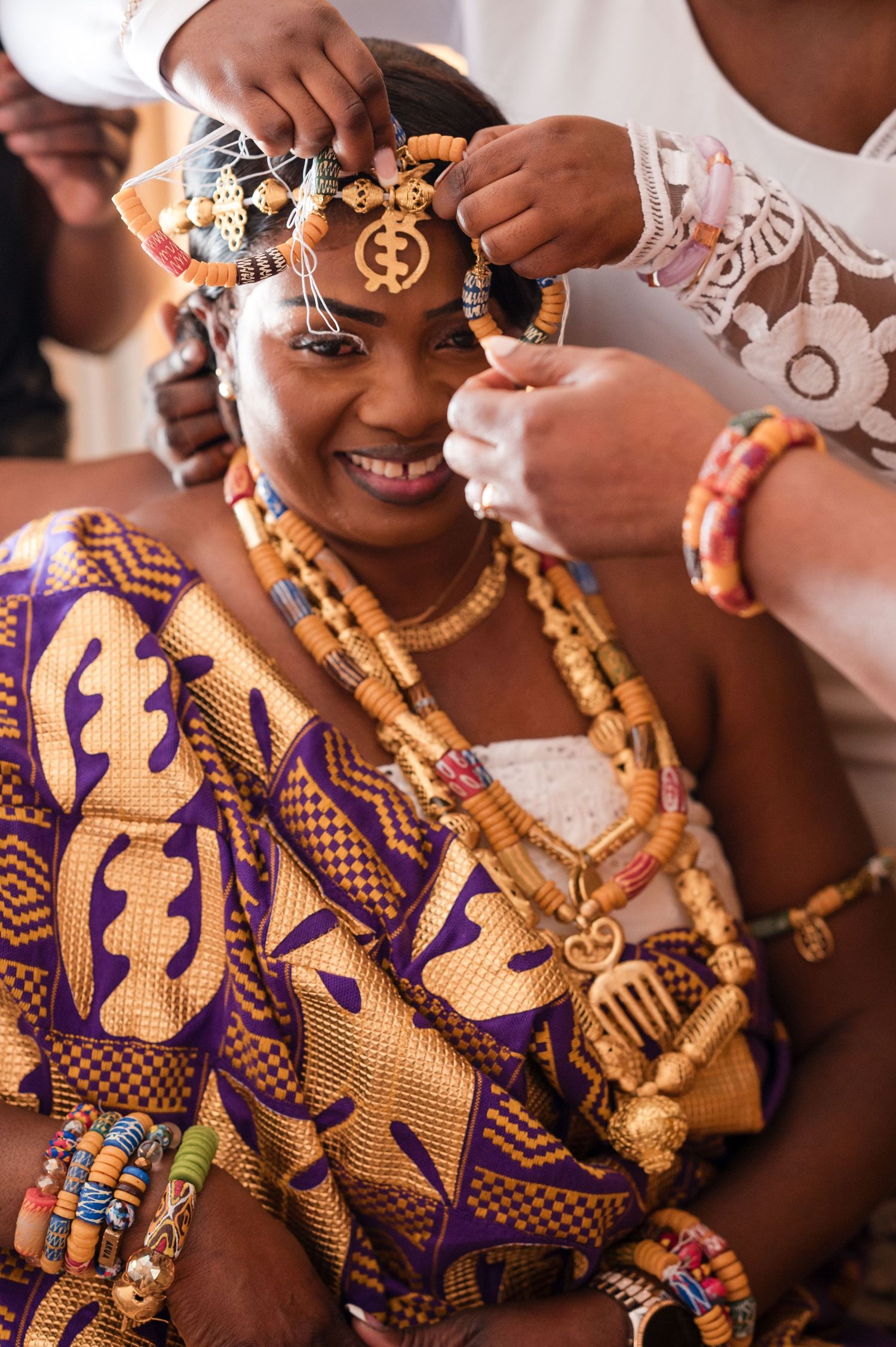 Traditional African wedding attire with vibrant purple and gold fabric, beaded necklaces and ornate jewelry.